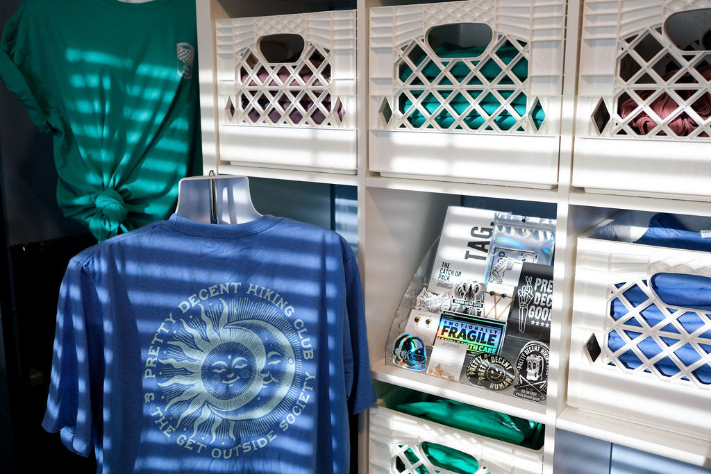 Blue t-shirt with a design on a hanger in front of white storage crates.